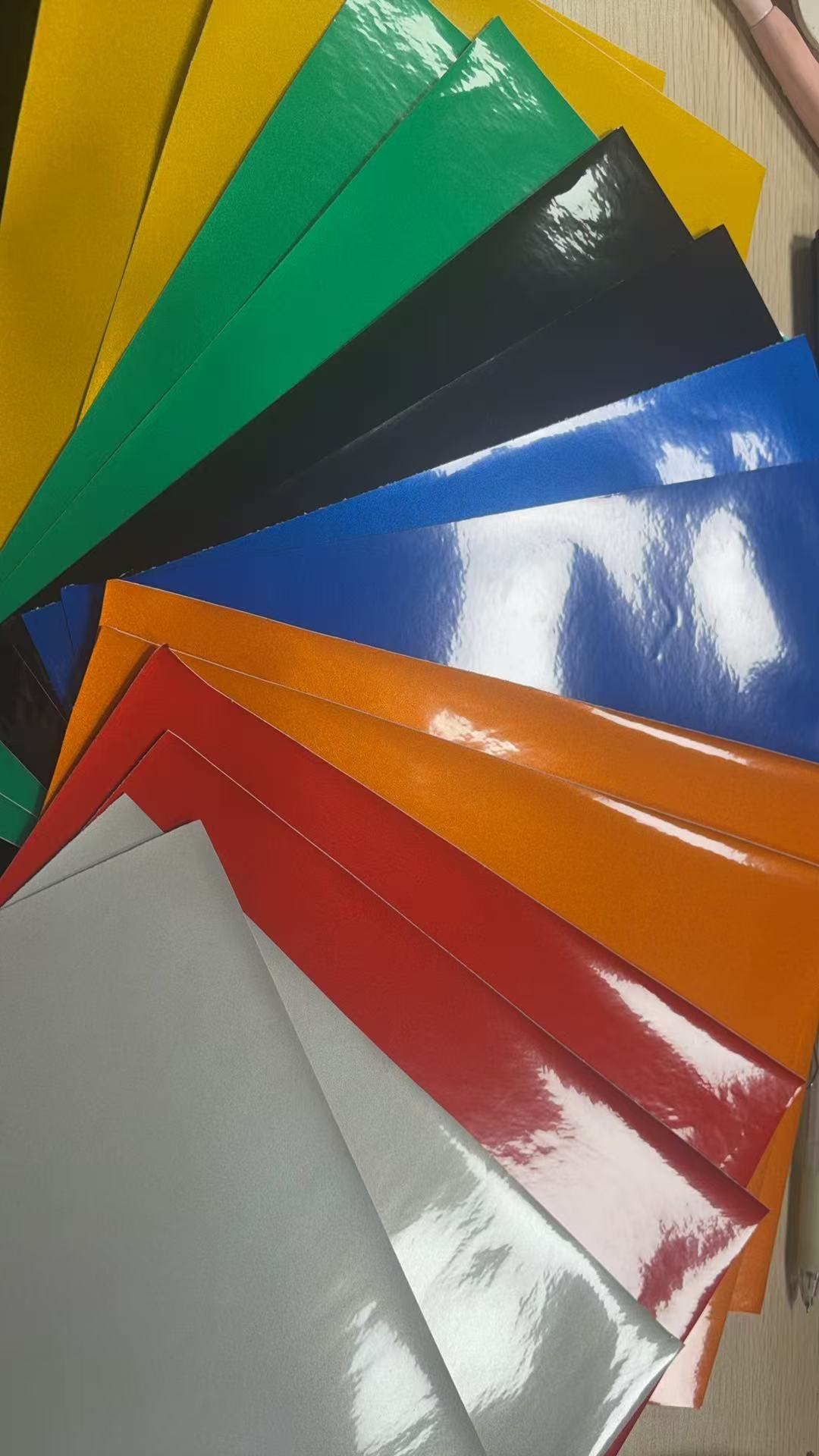 Colour samples of glass bead reflective sheeting fanned out showing yellow, green, black, blue, orange, red and silver options